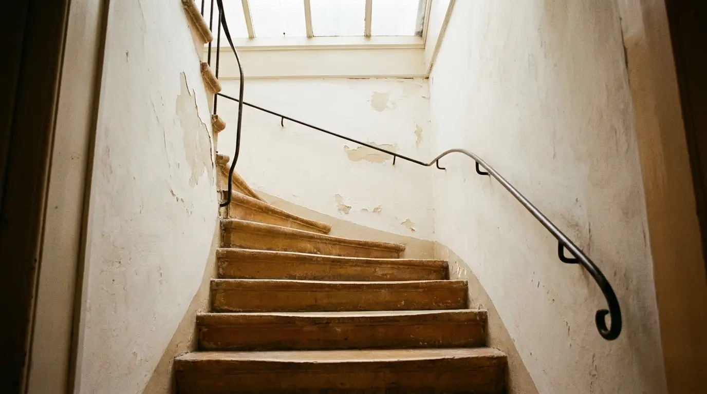 Enges, gewundenes Treppenhaus eines Altstadthauses mit ausgetretenen Holzstufen und schmiedeeisernem Handlauf, Tageslicht von oben.